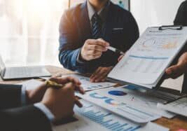 Young colleagues discuss business and analytical price charts using calculators and laptops to calculate financial, tax, accounting, statistics and analytical research ideas.