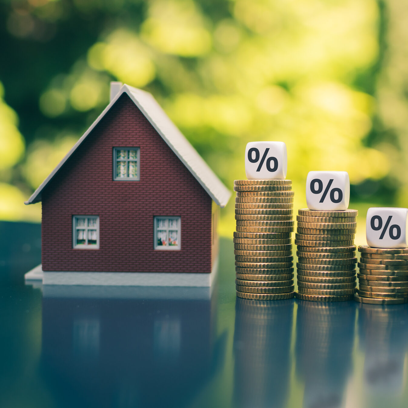 Symbol for decreasing interest rates. Dice with percentage symbols on decreasing high stacks of coins next to a model house.